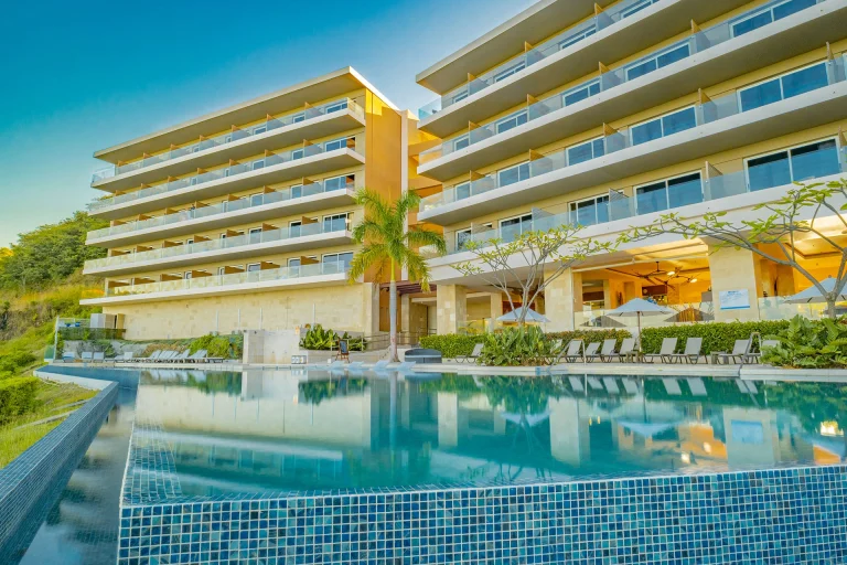 Fachada del hotel y piscina con palmeras, vista al mar_