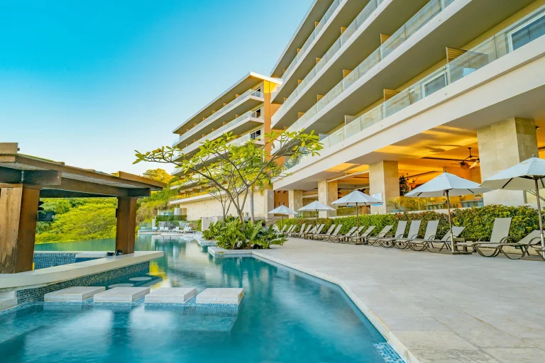 Piscina infinita frente al hotel, camastros y jardín_