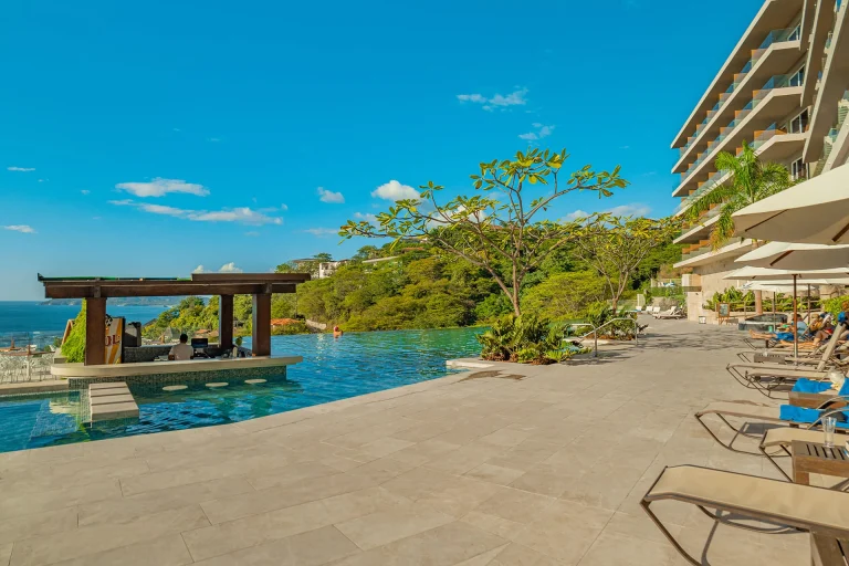 Terraza con camastros, jardines y piscina infinita_