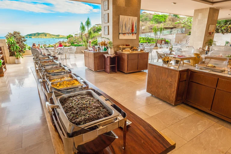 Línea de buffet caliente con variedad de platillos en salón amplio y luminoso